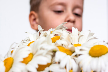Obraz na płótnie Canvas A cute boy with a beautiful bouquet of large daisies. Portrait of a child, funny and cute facial expression. Selective focus.