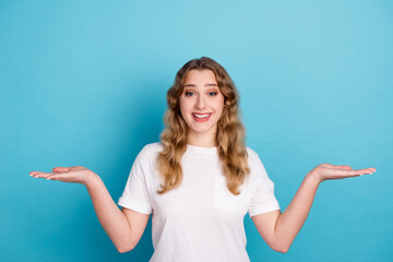 Portrait of nice cheery brown-haired girl holding palms copy space choosing options isolated over blue color background