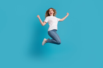 Fototapeta na wymiar Girl in white T-shirt and jeans jumping fist up victory on blue background