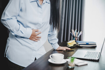 Young asian business woman person sitting at work and has stress pain in her stomach. Concept office syndrome abdomen pain from occupational disease, Female having belly pain and using laptop computer