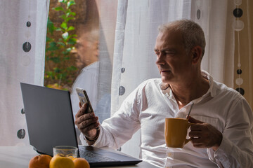 adult man working with pc and mobile phone while having breakfast at home