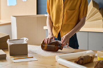 Close-up of female worker wrapping glass jar in packet to pack it in the box for delivery