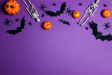 Halloween composition with pumpkins, spiders, bats and skeletons on purple background.