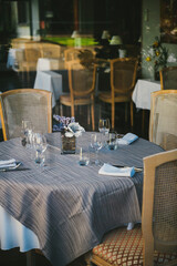 Glasses, napkins, flowers, fork, knife, all set ready to serve dinner in restaurant with cozy interior defocused background. Celebration, wedding decorations - useful file for catering services and