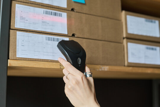 Close-up of woman scanning barcodes on parcels with scanner while working in warehouse
