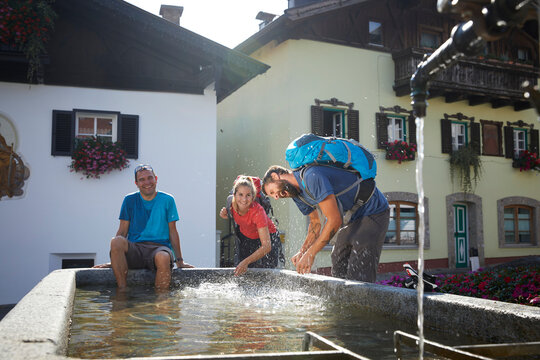 Happy hiker sitting by playful friends splashing water at fountain in village, Mutters, Tyrol, Austria