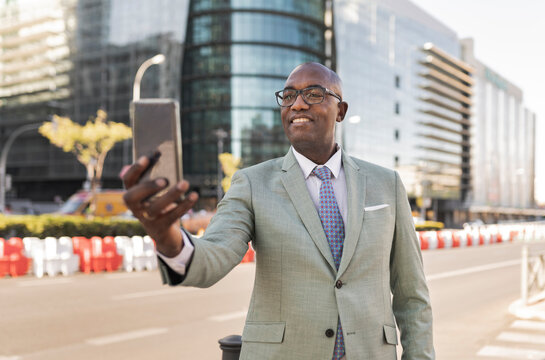 Smiling mature businessman taking selfie through smart phone on street