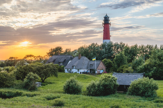 Germany, Schleswig-Holstein, Pellworm, Farmhouses in front of Pellworm Lighthouse at springtime sunset