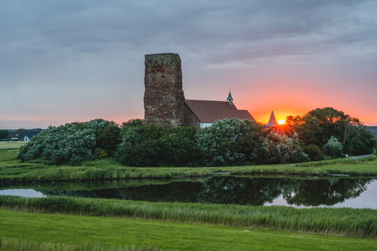 Germany, Schleswig-Holstein, Pellworm, Lake in front of Old Church of Saint Salvator at sunrise