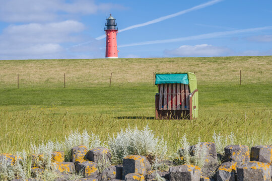 Germany, Schleswig-Holstein, Pellworm, Hooded beach chair with rock formation in foreground and Pellworm Lighthouse in background