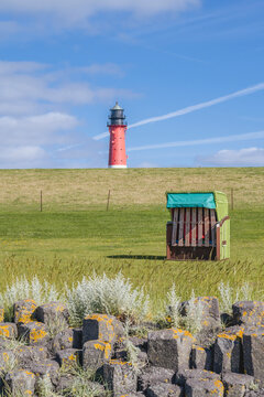 Germany, Schleswig-Holstein, Pellworm, Hooded beach chair with rock formation in foreground andPellworm Lighthouse in background