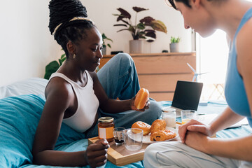 Smiling lesbian couple having breakfast on bed at home
