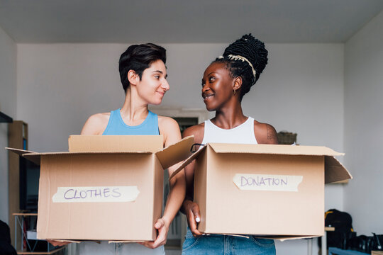 Smiling lesbian couple carrying boxes at home
