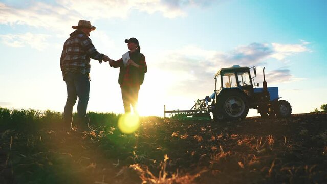 Deal in agribusiness. Two farmers discussing a deal against the background of a sunset. Business of farmers in a wheat field. Agriculture sale harvest concept. Silhouettes at sunset.