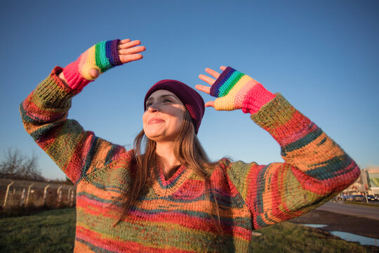 Smiling woman wearing rainbow gloves shielding eyes on sunny day