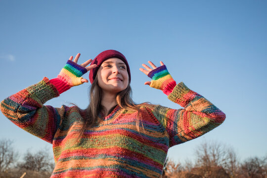 Smiling woman wearing rainbow gloves standing in front of clear sky