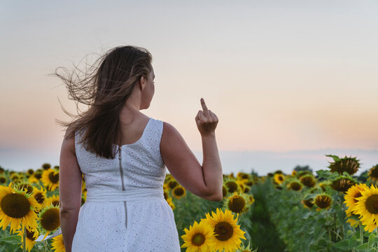 Woman gesturing middle finger at sunflower field