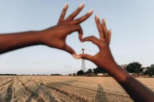 Woman making heart shape with hands in front of sky at farm