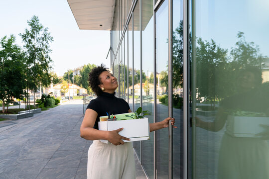 Smiling businesswoman holding box opening glass door
