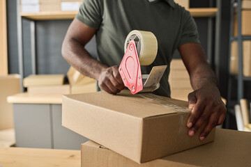 Close-up of African man packing cardboard box with adhesive tape in storage room