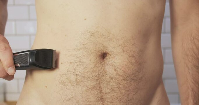 Man removes hair on his belly with an electric clipper, trimmer. Front view, close-up, bathroom.