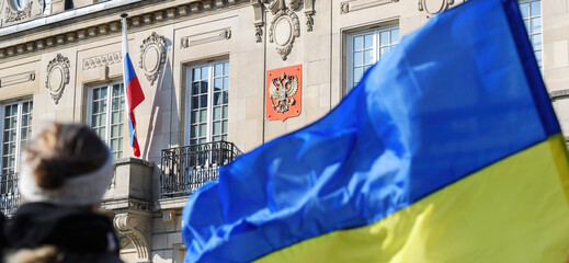 Ukrainian flag waving in front of Russian Flag and coat of arms on the Russian Consulate in...