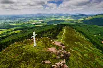 Wandcirkels tuinposter Tall white Catholic cross on top of Devils bit mountain in county Tipperary, Ireland. Aerial view. Beautiful landscape with green fields and forests in the background. Irish landscape. © mark_gusev