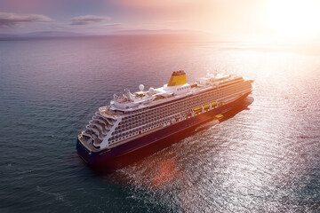 Big luxury cruise ship sailing along a cost. Blue cloudy sky Sunset sun in the background. Calm...
