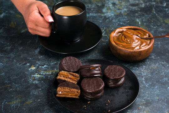 Alfajores with dulce de leche against person holding cup