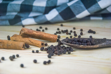 Cinnamon stick with black pepper seeds on wooden table