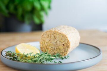 Raw Tempeh or Tempe, made of fermented soybean seeds on the plate on the kitchen table. Soya protein. Plant based meat concept. Healthy eating. Go vegan. Selective focus, copy space.