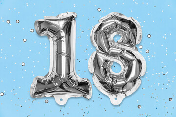 Silver foil balloon number, digit eighteen on a blue background with sequins. Birthday greeting card with inscription 18. Anniversary concept. Top view. Numerical digit. Celebration event, template.
