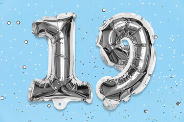 Silver foil balloon number, digit nineteen on a blue background with sequins. Birthday greeting card with inscription 19. Top view. Numerical digit. Celebration event, template.