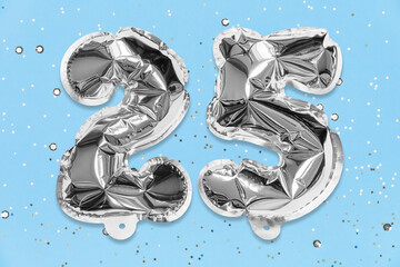 Silver foil balloon number, digit twenty five on a blue background with sequins. Birthday greeting card with inscription 25. Anniversary concept. Numerical digit. Celebration event, template.