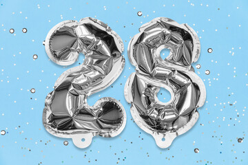 Silver foil balloon number, digit twenty eight on a blue background with sequins. Birthday greeting card with inscription 28. Top view. Numerical digit. Celebration event, template.