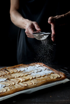 Crop baker sprinkling pie with powdered sugar