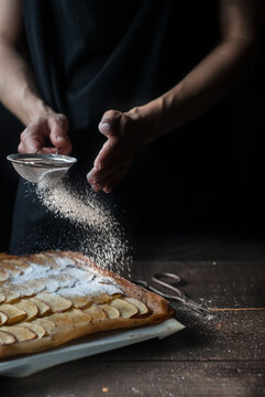 Crop baker sprinkling pie with powdered sugar