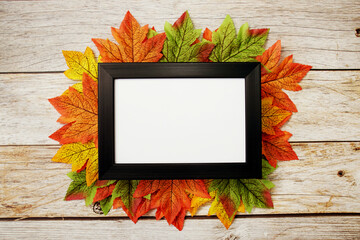 Empty mock up photo frame with maple leaves on wooden background