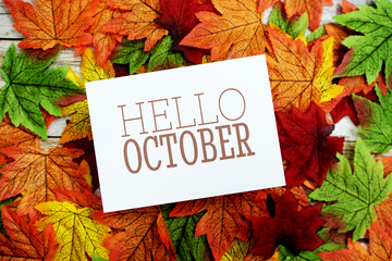 Hello October text message with maple leaves on wooden background