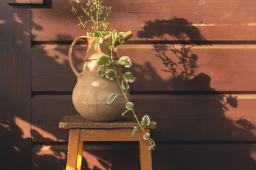A bouquet of meadow flowers in a clay vase in the rays of the setting sun against the background of the wall of a wooden summer log house. Summer background