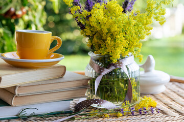 Bouquet of meadow flowers, cup of tea or coffee, books on table in summer garden. Relaxing, reading...