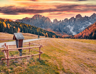 Photographet walks on the country road in Venegia valley, high altitude Dolomite valley natural park with jagged peaks, rolling meadows, pastures and streams. Sunrise in Italian countryside.