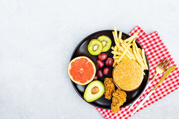 Flat lay of Healthy and unhealthy food from fruits and vegetables vs fast food, sweets and pastry in black plate on gray concrete background. Diet and detox against calorie and overweight lifestyle