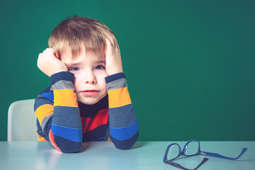 A tired boy sits at his desk, holding his head in his hands. Close-up