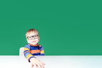 Funny boy with glasses sitting at the table. Copy space