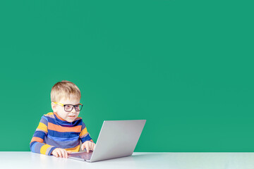 Joyful boy with glasses plays in the laptop. Copy space