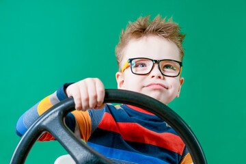 Dreamy boy holding the wheel in his hands in the studio on a green background. Close-up