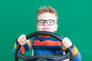 Cheerful boy playing with the steering wheel, on a green background in the studio. Close-up