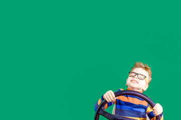 Dreaming boy holds steering wheel in hand, on green background in studio