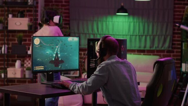Gamer playing multiplayer space shooter while gaming girl is fighting in virtual reality game at home. Man streaming online action game on pc while gaming girl uses vr goggles for simulation.